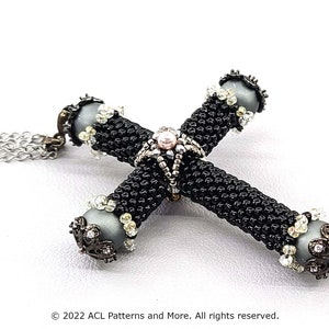 May include: A beaded cross pendant necklace. The cross is black with grey orbs at the ends, adorned with clear crystals and ornate metalwork. A silver chain supports the cross, creating a striking accessory.
