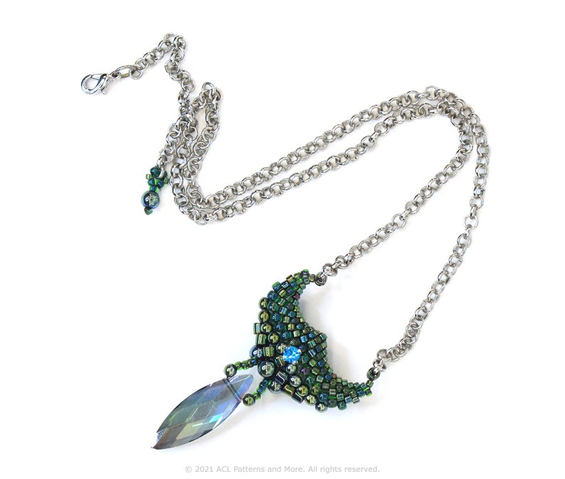 May include: A silver chain necklace with a green and blue beaded pendant. The pendant is shaped like a crescent moon with a teardrop-shaped crystal hanging from the bottom.