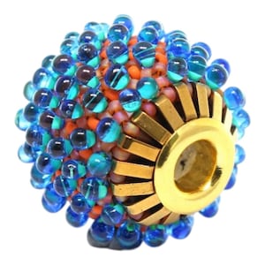 May include: A decorative bead with a gold-colored metal end cap. The bead is covered in small, round, blue and teal glass beads. The center of the bead is orange and pink. This bead is suitable for jewelry making.