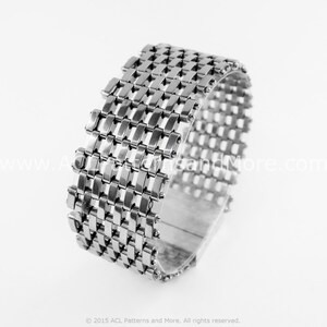 May include: A silver metal bracelet with a woven design. The bracelet is made of small, interconnected metal links that create a grid-like pattern.
