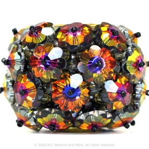 May include: A round, multi-faceted bead made of iridescent glass. The bead is composed of many small, flower-shaped pieces in shades of orange, yellow, purple, and black.