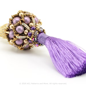 Op de afbeelding: Een paarse en gouden kralenkwast met een paarse kwast. Het kralen gedeelte is gemaakt van kleine, ronde kralen en heeft een gouden metalen accent.