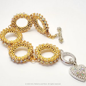 May include: A gold beaded bracelet with a heart-shaped charm. The bracelet is made of multiple linked circles of gold beads with iridescent accents. The heart charm is silver with a clear crystal design.