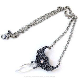 May include: A silver chain necklace with a black beaded crescent moon pendant and a clear crystal teardrop hanging from the bottom.