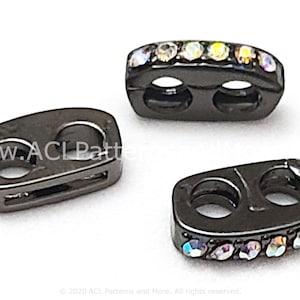 May include: Three black metal toggle clasps with two holes each. Two clasps have a row of iridescent rhinestones. The clasps are used for clothing, bags, and other crafts.