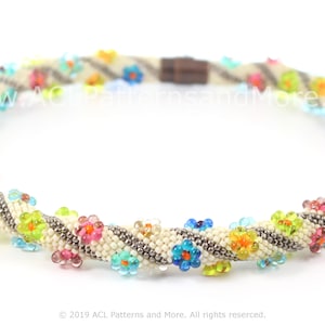 May include: A beaded necklace with a spiral design. The necklace features small, colourful flower accents in shades of blue, pink, yellow, and green. The base is cream-coloured with a brown magnetic clasp. The text "ACL Patterns and More" is visible.