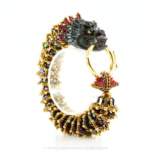 May include: A gold and iridescent beaded bracelet with a dragon head clasp. The dragon is made of metal and has green eyes. The bracelet is made of small beads in shades of gold, red, and blue.