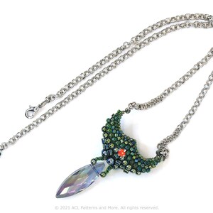 May include: A silver chain necklace with a green and blue beaded pendant. The pendant is shaped like a crescent moon with a crystal teardrop hanging from the bottom.