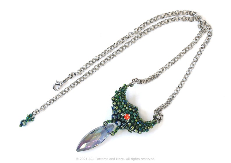 May include: A silver chain necklace with a green and blue beaded pendant. The pendant is shaped like a crescent moon with a crystal teardrop hanging from the bottom.