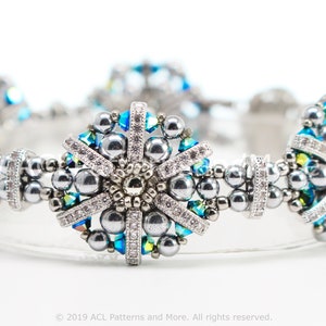 May include: A silver and blue beaded bracelet featuring a snowflake design. The bracelet is crafted with small, round beads and has a delicate, intricate design.