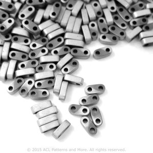 Peut inclure: Un grand tas de perles en métal argenté avec deux trous dans chaque perle. Les perles sont éparpillées sur une surface blanche.