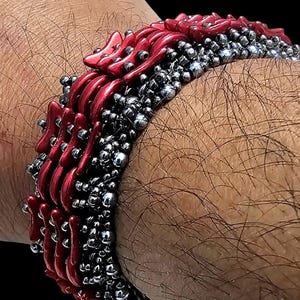 May include: A red and silver beaded bracelet with a unique design. The bracelet is made of small, round beads and features a pattern of interlocking stars.