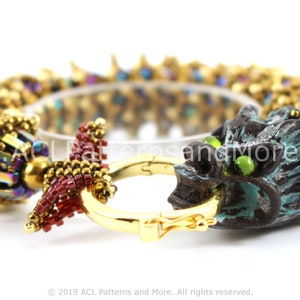 Könnte beinhalten: Ein Armband mit Perlen und einem Drachenkopf-Anhänger. Das Armband ist aus goldenen, roten und blauen Perlen gefertigt. Der Drachenkopf-Anhänger ist aus einem dunkelblauen und grünen Material.