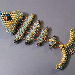 May include: A beaded fish skeleton necklace with a blue and gold colour scheme. The necklace features a detailed fish skeleton design with a small blue bead for an eye.