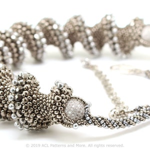 May include: A silver and gray beaded necklace with a spiral design. The necklace has a silver clasp and a large silver bead with a clear crystal center.