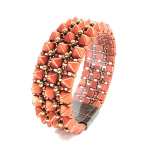 May include: A copper-coloured beaded bracelet with a geometric design. The bracelet features pyramid-shaped beads and small gold-coloured beads. The bracelet is made of multiple rows of beads and has a magnetic clasp.