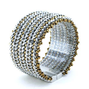 May include: A silver and gold beaded bracelet with a magnetic clasp. The bracelet is made of small, round beads that are woven together in a herringbone pattern.