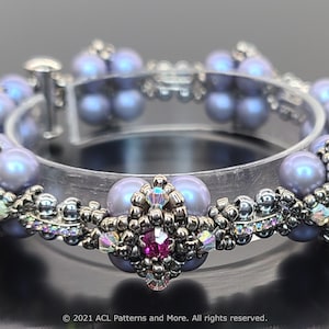 May include: A silver and lavender beaded bracelet with a crystal accent. The bracelet is made with small seed beads and larger pearl-like beads.