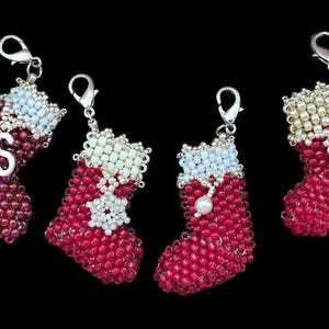 May include: Four beaded Christmas stocking charms in red, white, and silver. Each charm has a silver clasp and a white beaded cuff. One stocking has the letter "S", another has a snowflake, another has a pearl, and the last has the letter "R".