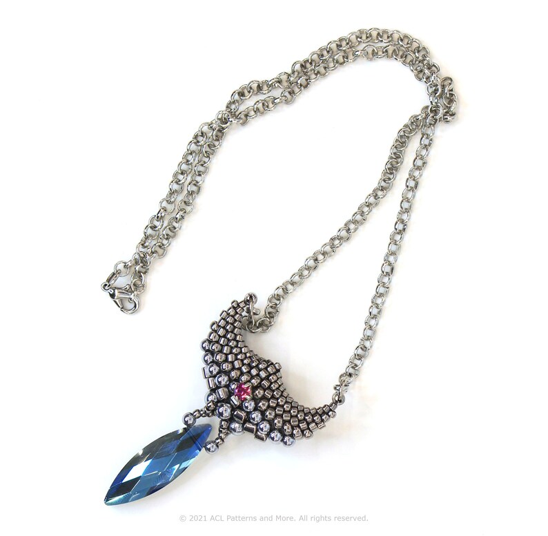 May include: A silver chain necklace with a silver and blue pendant. The pendant is shaped like a crescent moon with a teardrop-shaped blue crystal hanging from the bottom.