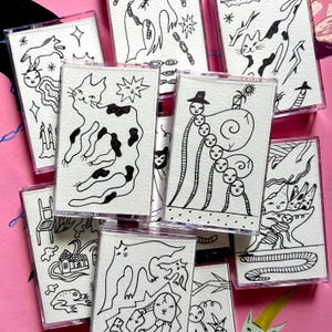 May include: A collection of cassette tapes with unique, hand-drawn black and white illustrations. The artwork features various whimsical designs, including cats, figures, and abstract patterns. The tapes are encased in clear plastic.