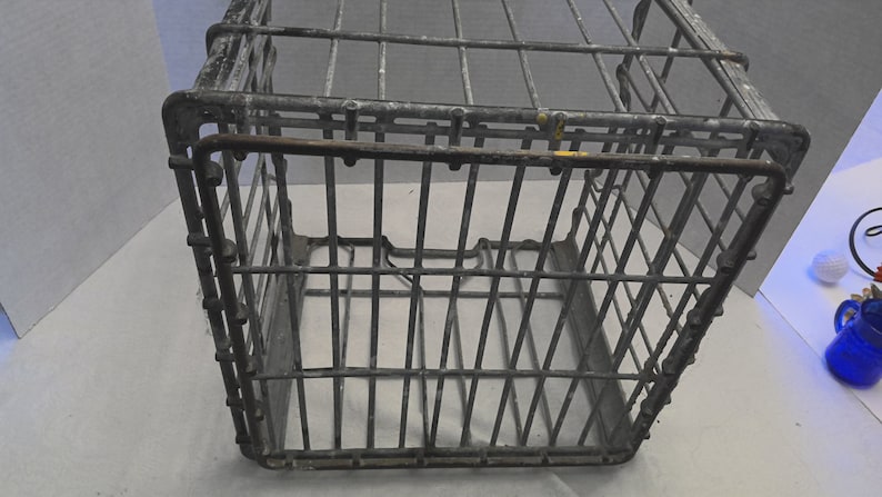 Puede incluir: Una caja de alambre de metal vintage con forma rectangular. La caja est&aacute; hecha de malla de alambre y tiene un asa en la parte superior. La caja es gris y tiene algunas manchas de &oacute;xido.