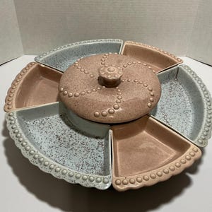 May include: A vintage serving dish with a central lidded compartment and six surrounding sections. The dish is in shades of pink and blue with a speckled finish and a beaded edge. The lid has a decorative knob.