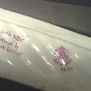 May include: An off-white ceramic piece with the text "Irish setter" and "Modelled by Doris Lindner" in red ink. A pink crest and the number 3228 are also visible. The piece is rectangular.