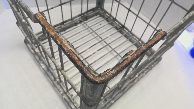 Puede incluir: Una caja de alambre de metal cuadrada con bordes oxidados. La caja est&aacute; hecha de alambre de metal delgado y tiene un acabado gris. La caja est&aacute; vac&iacute;a.