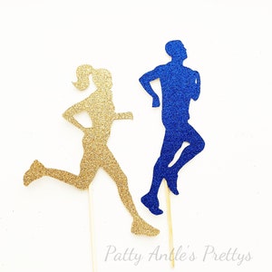 May include: Two glitter running figures, one gold and one blue, on wooden sticks. The figures are silhouetted and are running in opposite directions. The text "Patty Antle's Prettys" is at the bottom of the image.