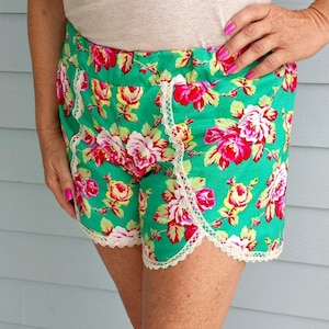 May include: Green floral shorts with white lace trim. The shorts have a pink and red floral pattern.