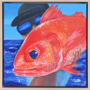 May include: A framed painting depicting a large, red fish held by a person wearing sunglasses and a hat. The background shows a blue sky and sea. The artwork is square and the fish is the central subject.