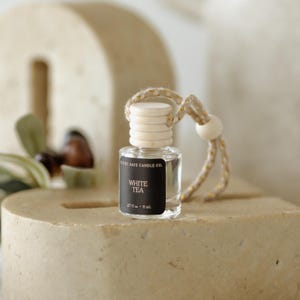 May include: A small, clear glass bottle with a wooden cap and a black label that reads "WHITE TEA". The bottle is suspended by a beige string with a wooden bead. The bottle contains 0.27 fl oz or 8 ml of liquid.