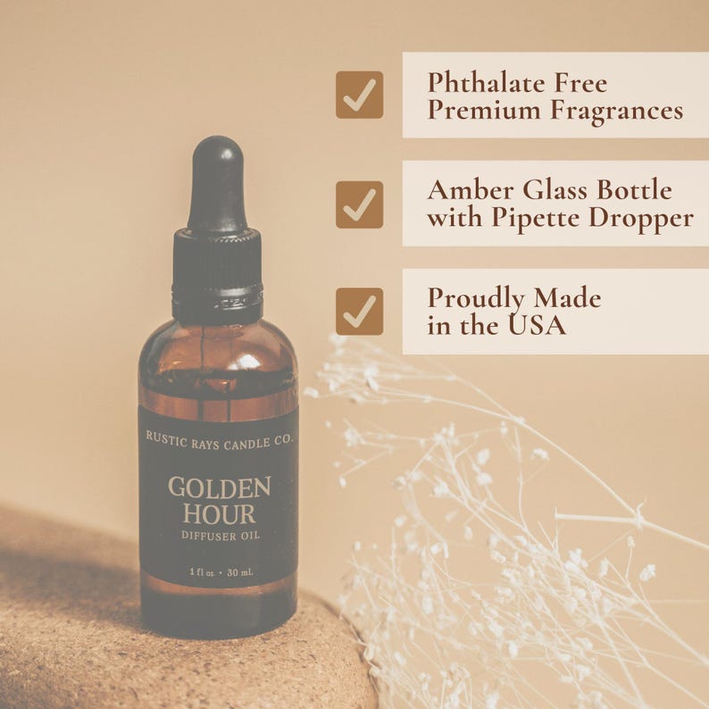 Puede incluir: Una botella de vidrio marr&oacute;n con un gotero negro y una etiqueta que dice "RUSTIC RAYS CANDLE CO. GOLDEN HOUR DIFFUSER OIL 1 fl oz - 30 ml". La botella est&aacute; sobre una superficie marr&oacute;n con flores blancas en el fondo. La imagen tambi&eacute;n incluye tres marcas de verificaci&oacute;n con texto al lado: "Phthalate Free Premium Fragrances", "Amber Glass Bottle with Pipette Dropper", y "Proudly Made in the USA".