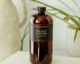 Może przedstawiać: Brązowa plastikowa butelka z czarną nakrętką i czarną etykietą z napisem Rustic Rays Candle Co. Sea Salt & Orchid Air + Linen Spray 16 fl oz 473 mL. Butelka ma cylindryczny kształt i gładkie, odblaskowe wykończenie powierzchni.