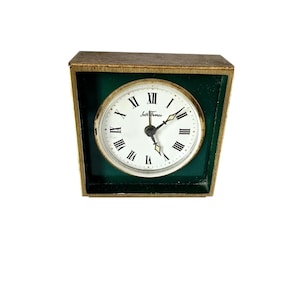 May include: A vintage Seth Thomas clock with a gold-toned frame and a green interior. The clock face is white with black Roman numerals and hands. The clock measures approximately 4 inches wide and 4 inches tall.