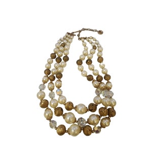 May include: A three-strand necklace with gold, white, and clear beads. The necklace is made of faux pearls, gold-toned beads, and clear crystal beads.