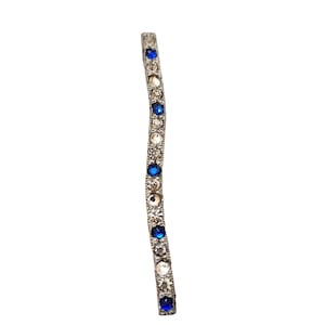 May include: A silver-toned hair barrette with a wavy design. The barrette is adorned with clear and blue rhinestones.