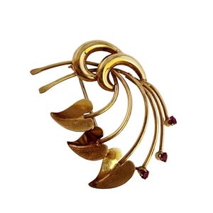 May include: A gold-toned brooch with a swirling design and five red gemstones. The brooch features a stylised leaf motif.