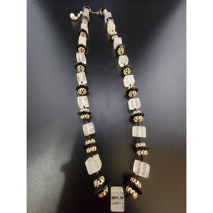 May include: A vintage necklace featuring clear, square-cut beads interspersed with black and gold-toned decorative elements. The necklace has a delicate chain and a small pearl accent near the clasp. The design is symmetrical and elegant.