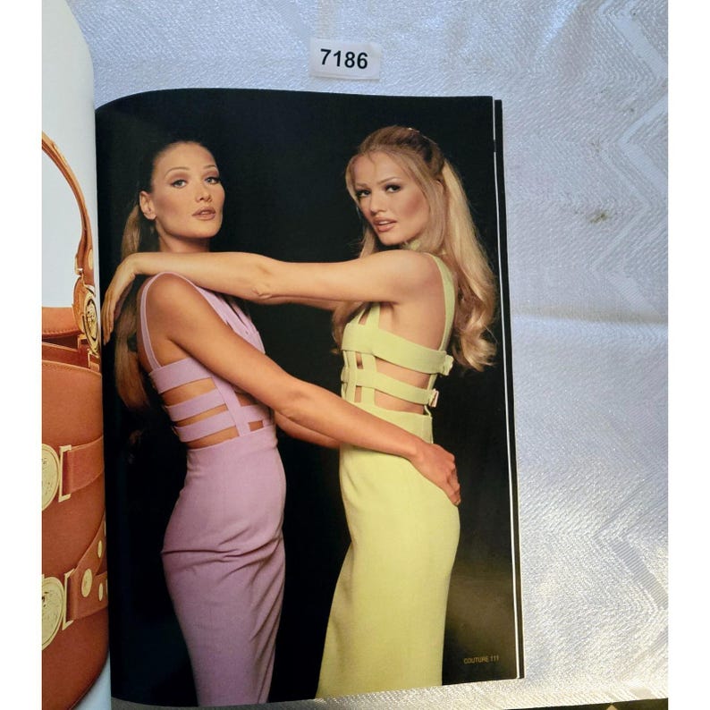 May include: Two models in a fashion editorial, wearing figure-hugging dresses. One dress is a pale lavender, the other a pale yellow-green. Both dresses feature cut-out details across the bodice and back. The background is black.
