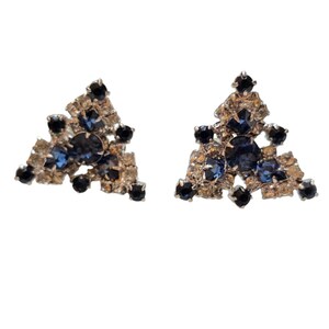 May include: A pair of vintage stud earrings. Each earring features a triangular design with a silver-tone metal setting. The earrings are adorned with a combination of clear, dark blue, and black rhinestones, creating a sparkling effect.