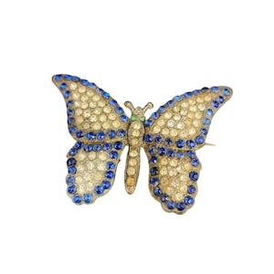 Puede incluir: Un broche de mariposa de tono dorado con diamantes de imitación transparentes y azules. La mariposa tiene un diseño detallado y es de estilo vintage.