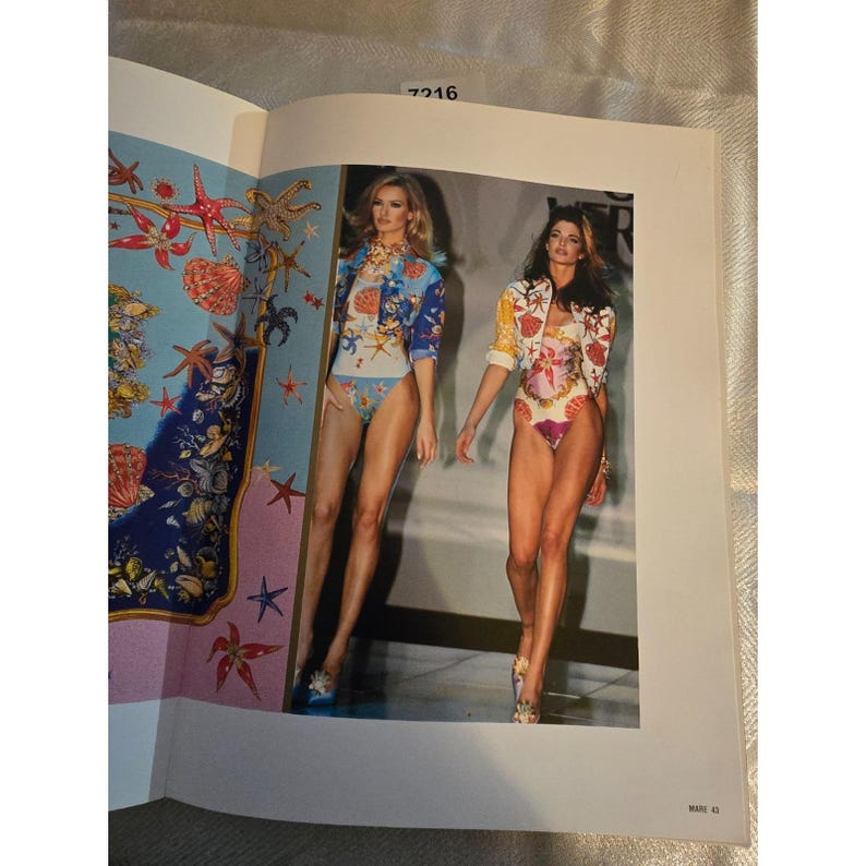 May include: A fashion magazine page featuring two models wearing colorful swimwear and jackets. The outfits have seashell and floral patterns. The model on the left wears a blue jacket and swimsuit, while the other wears a yellow and red jacket and swimsuit.