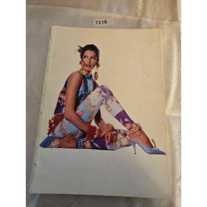 May include: A fashion magazine cover featuring a woman in a colorful outfit. She wears a sleeveless top and leggings with a sea-themed print. Her accessories include large earrings and blue heels. The magazine has the number 7216 in the top right corner.