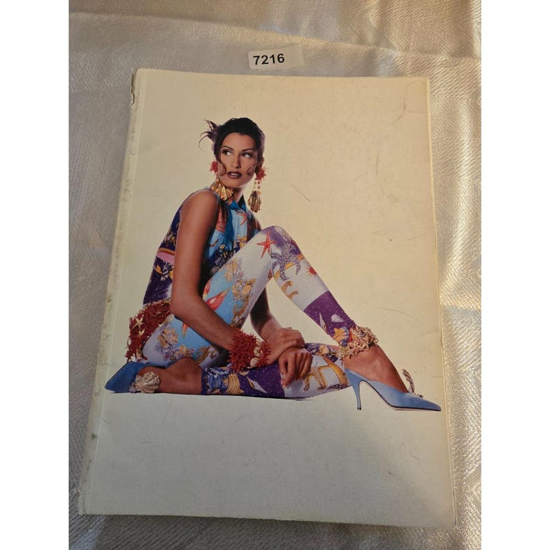 May include: A fashion magazine cover featuring a woman in a colorful outfit. She wears a sleeveless top and leggings with a sea-themed print. Her accessories include large earrings and blue heels. The magazine has the number 7216 in the top right corner.