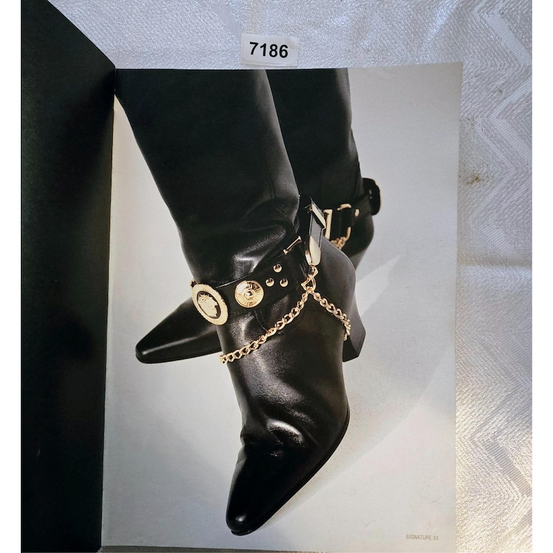 May include: Black leather boots with pointed toes and gold-tone chain and medallion details. The boots have a mid-height heel and an ankle strap. The image shows the boots from the knees down.