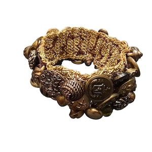 May include: A gold-toned bracelet featuring a woven gold chain center and an array of vintage buttons. The buttons vary in size and design, with intricate details and a mix of textures. The bracelet has a unique, handcrafted appearance.