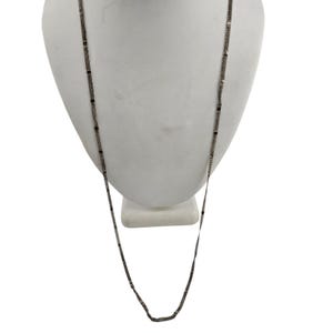 May include: A long, dark gray necklace with small, dark beads. The necklace is displayed on a white bust against a white background. The chain is made of small, rectangular links.