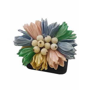 Puede incluir: Un broche de flor colorido con un grupo de cuentas blancas en el centro. La flor está hecha de tela y tiene pétalos en tonos de rosa, azul, verde y amarillo.